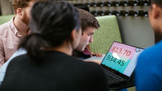 Screenshot that shows a group of people looking at a magnified computer screen.
